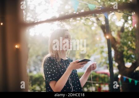 Jeune femme souriante parlant à travers des écouteurs dans le balcon pendant la fête Banque D'Images