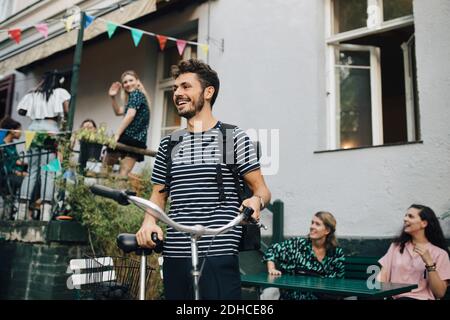 Jeune homme souriant debout avec un vélo dans l'arrière-cour Banque D'Images