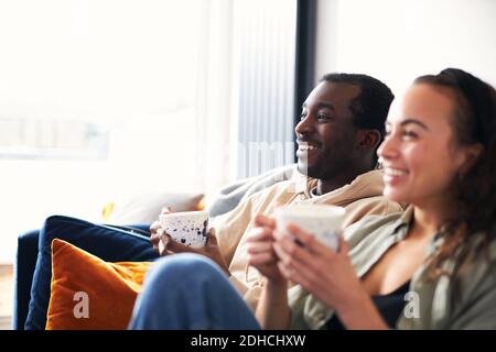 Jeune couple mixte d'ethnie se détendant sur le canapé à l'observation de la maison ou diffuser la télévision en streaming Banque D'Images