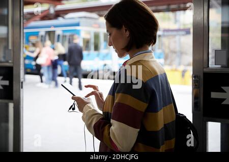 Femme d'affaires utilisant un smartphone en se tenant à la gare Banque D'Images