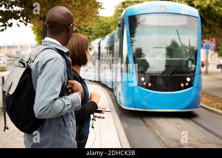 Les voyageurs qui attendent sur le trottoir tout en regardant le tram bleu à l'intérieur ville Banque D'Images