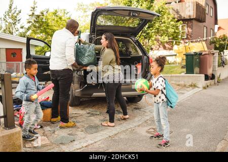 Les frères et sœurs jouent pendant que les parents chargent leurs bagages dans le coffre de la voiture allée Banque D'Images