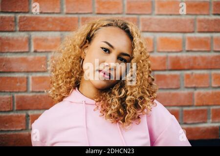 Portrait de la jeune femme avec les cheveux bouclés contre le mur de brique Banque D'Images