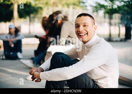 Portrait d'un jeune homme heureux assis avec des amis à la planche à roulettes stationnement Banque D'Images