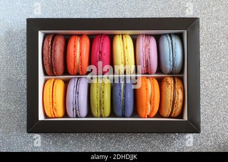 Macarons multicolores dans une boîte en carton sans couvercle sur une surface argentée à paillettes. Vue de dessus. Gros plan Banque D'Images