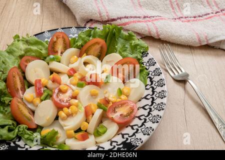 Salade fraîche et exquise de cœurs de palmier coupés en tranches, tomates cerises, grains de maïs, poivron rouge, laitue dans une assiette bleu clair vintage sur un bois Banque D'Images