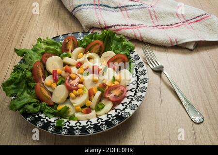 Salade fraîche et exquise de cœurs de palmier coupés en tranches, tomates cerises, grains de maïs, poivron rouge, laitue dans une assiette bleu clair vintage sur un bois Banque D'Images