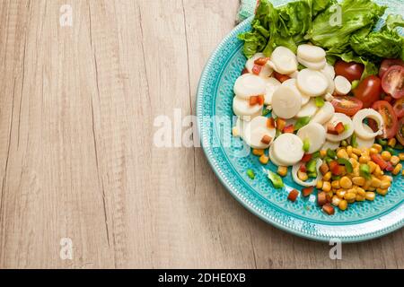 Salade fraîche et exquise de cœurs de palmier coupés en tranches, tomates cerises, grains de maïs, poivron rouge, laitue dans une assiette bleu clair vintage sur un bois Banque D'Images