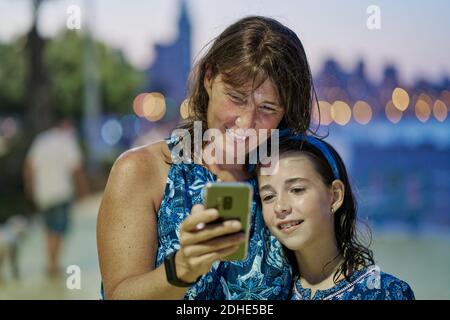 Portrait de la mère et de la fille adolescente portant des robes bleues et regardant le mobile la nuit avec une plage en arrière-plan. Concept de technologie Banque D'Images