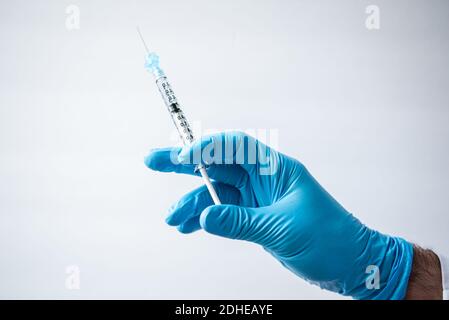 Main dans le gant tenant une seringue avec un vaccin sur fond blanc. Banque D'Images