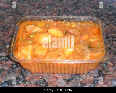 retirez la viande de veau mijotée avec les pommes de terre, les petits pois verts dans la sauce tomate dans un plateau en plastique avec un fond en granit foncé Banque D'Images