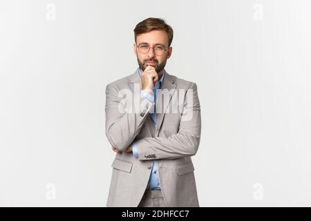 Portrait d'homme d'affaires barbu réfléchi en lunettes et costume gris, prenant sa décision, en vous calmant et en vous regardant, en pensant Banque D'Images
