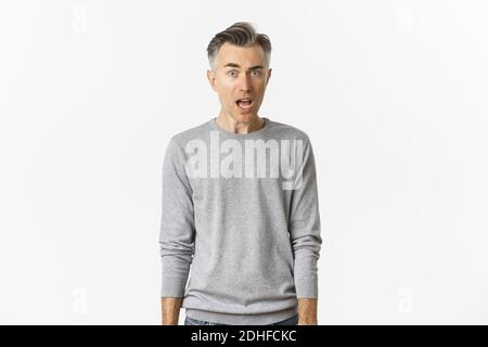 Portrait d'un beau homme d'âge moyen avec des cheveux gris, en regardant confus et surpris, bouche ouverte et regarder la caméra, debout ove Banque D'Images
