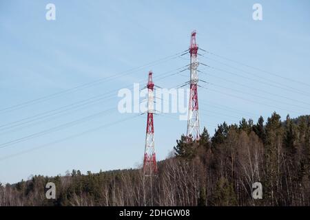 Supports métalliques de lignes électriques aériennes pour l'électricité, dans la colline de la forêt, sur fond bleu ciel. Banque D'Images