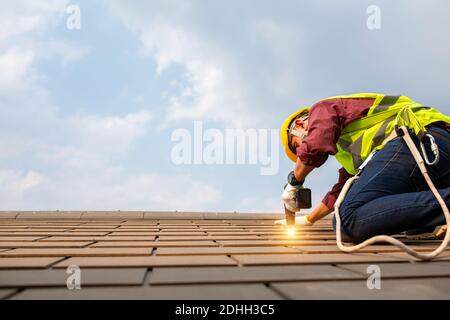 Réparation de toit, installation de toit par un travailleur de la construction, Outils de couverture, perceuse électrique utilisée pour remplacer les plaques de toit qui ont été utilisées depuis longtemps. Banque D'Images
