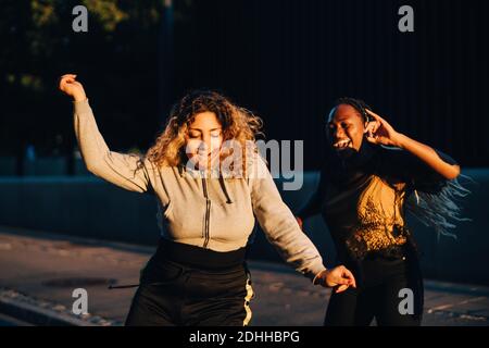 Des amis enthousiastes dansant au parc de skateboard pendant le coucher du soleil Banque D'Images