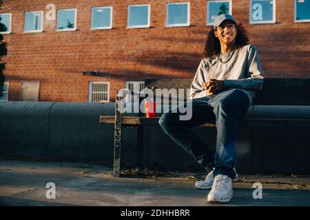 Homme heureux regardant loin en étant assis sur le banc contre le bâtiment Banque D'Images