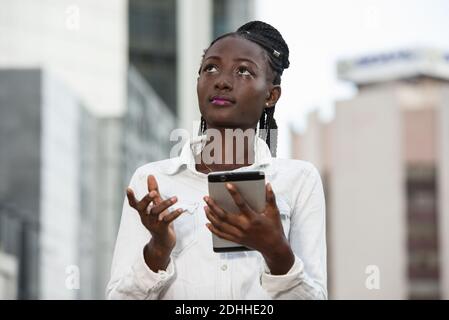 Gros plan portrait jeune femme d'affaires regardant de côté et questionnant mobile téléphone dans la ville Banque D'Images