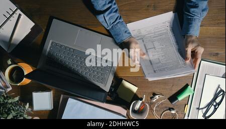Homme d'affaires assis au bureau et travaillant, il vérifie la paperasse et utilise son ordinateur portable, vue de dessus Banque D'Images