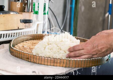 Placez le riz gluant cuit à la vapeur sur un plateau en bambou pour permettre à la chaleur de se répandre. Banque D'Images