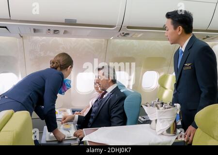 Compagnie aérienne d'hôtesse d'air en avion servant de la nourriture à l'homme d'affaires en classe affaires dans la cabine passager dans l'avion. Banque D'Images