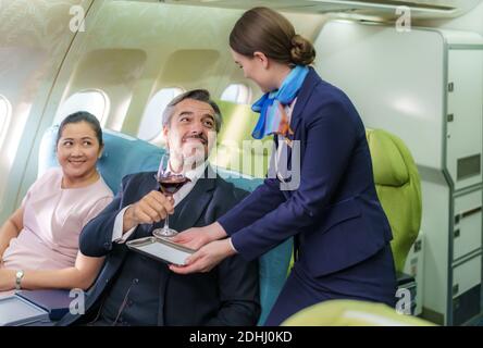 Compagnie aérienne d'hôtesse d'air dans un avion servant du vin rouge à un homme d'affaires en classe affaires dans une cabine passager dans un avion. Banque D'Images