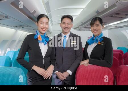 Portrait de trois hommes et femmes en costume bleu accompagnateur/hôtesse d'air dans une cabine de classe économique souriant d'accueillir le passager à l'avion. Banque D'Images