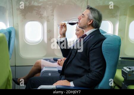 Pendant le vol, un homme d'affaires passager tenant un verre de vin mousseux et buvant en classe affaires dans une cabine d'avion. Banque D'Images