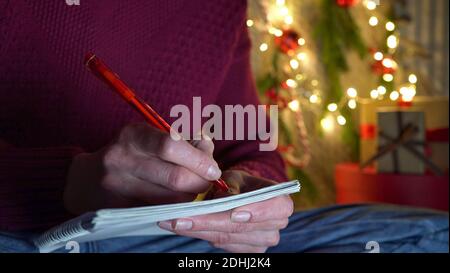 Femme dans un chandail rouge et jeans écrit une lettre avec un stylo rouge au Père Noël sur le fond du décor de Noël.gros plan. Banque D'Images