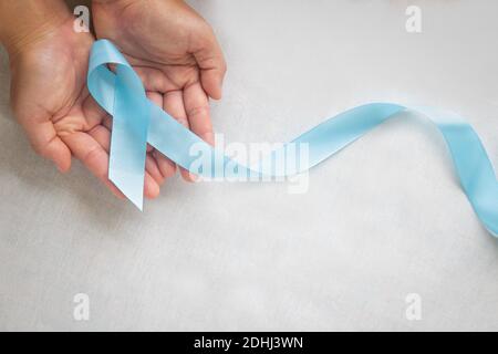 Main tenant le ruban bleu clair sur un arrière-plan blanc isolé avec espace de copie. Symbole mois de sensibilisation au cancer de la prostate et lymphoedème. Soins de santé m Banque D'Images