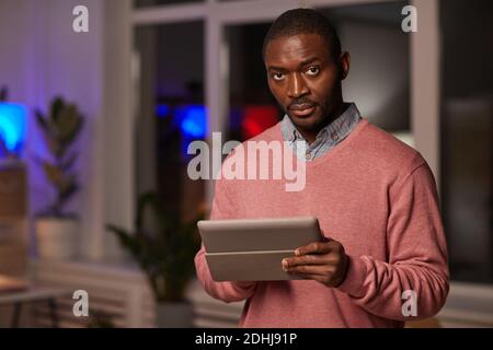 Portrait de l'homme beau africain regardant l'appareil photo pendant l'utilisation tablette numérique au bureau Banque D'Images