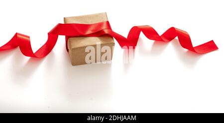 Saint-Valentin, cadeau de noël emballage maison, préparation des vacances. Faire un noeud avec un ruban de satin rouge, décoration d'une boîte cadeau en papier brun, isoler Banque D'Images