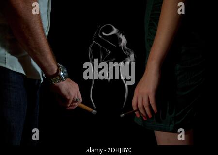 Homme et femme tenant des cigarettes la fumée forme une image d'un couple qui s'enserre Banque D'Images