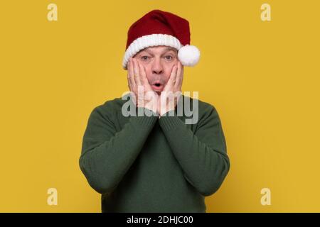 Un homme senior du père noël a été surpris de dire wow. Studio tourné sur un mur jaune. Banque D'Images