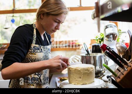 adolescente en cuisine appliquant du glaçage au gâteau Banque D'Images