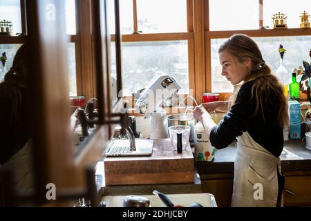 Adolescente dans une cuisine suivant une recette de pâtisserie sur un ordinateur portable. Banque D'Images