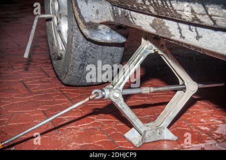 La voiture est soulevée à l'aide d'un cric et une clé de roue dépasse de la roue. Remplacement saisonnier des pneus sur fond de carreaux rouges Banque D'Images