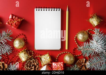 Bloc-notes et crayon pour écrire des voeux et des cadeaux pour le nouvel an et Noël autour des décorations d'arbre de Noël sur un fond rouge. Nouvel an moo Banque D'Images