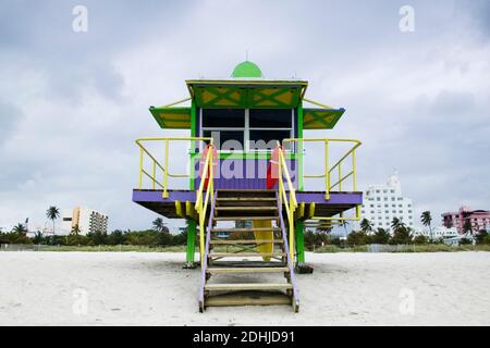 Refuge de sauveteurs en bois coloré sur une plage de sable avec des bâtiments élevés au-delà. Banque D'Images