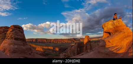 Randonneur méditant en appréciant les premiers rayons du soleil de la journée à Delicate Arch, parc national d'Arches. Magnifique lever de soleil avec vue imprenable sur le parc national d'Arches Banque D'Images