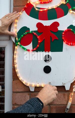 Gros plan sur les lumières de Noël domestiques pour les fêtes de fin d'année. Installation de la lampe bonhomme de neige sur le mur extérieur de la maison en hiver Banque D'Images