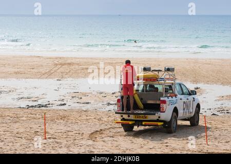 Un garde-corps RNLI debout à l'arrière d'un véhicule d'intervention d'urgence sur la plage de Fistral à Newquay, en Cornouailles Banque D'Images