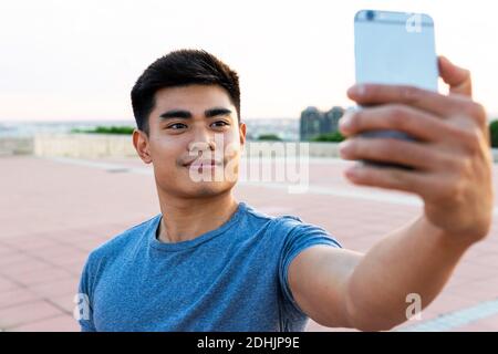 Beau homme asiatique debout en ville tout en prenant des photos selfie appareil photo de téléphone portable et sourire Banque D'Images