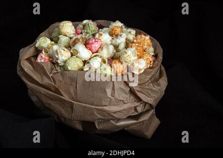 Tas de pop-corn doux aux couleurs varicolores dans un sac en papier placé avec graines de maïs jaune sur fond noir en studio Banque D'Images