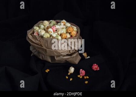 Tas de pop-corn doux aux couleurs varicolores dans un sac en papier placé avec graines de maïs jaune sur fond noir en studio Banque D'Images