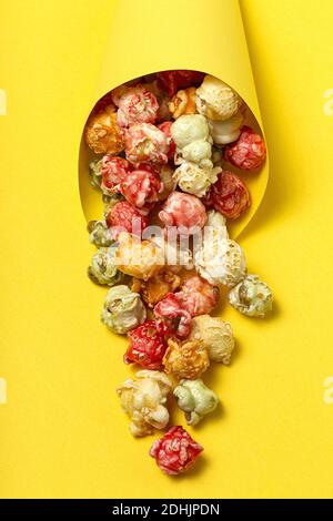 Grand angle de pop-corn savoureux coloré dans le cône en papier placé sur fond jaune en studio Banque D'Images