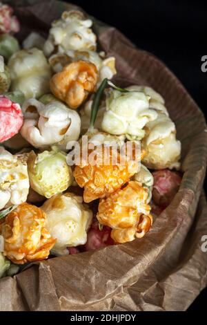 Tas de pop-corn doux aux couleurs varicolores dans un sac en papier placé avec graines de maïs jaune sur fond noir en studio Banque D'Images