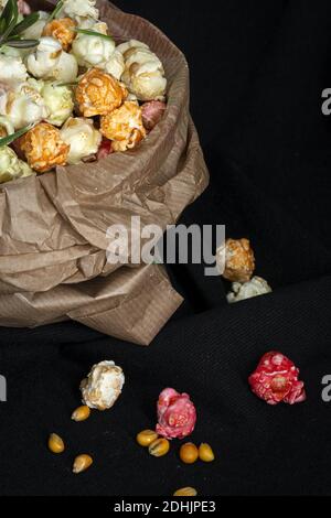 Grand angle de tas de pop-corn doux aux couleurs varicolores en papier sac placé avec des graines de maïs jaunes sur fond noir dans studio Banque D'Images