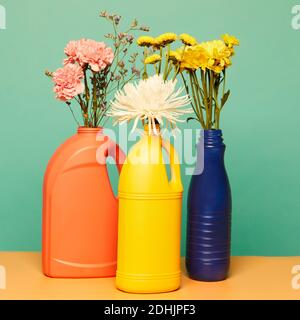Différentes fleurs en fleurs placées dans des bouteilles en plastique colorées de détergents présentation du concept de conteneurs réutilisables Banque D'Images