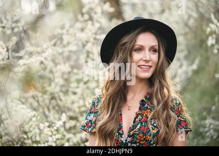 Femme douce en robe longue marchant dans le parc de printemps parmi arbres et buissons en fleurs Banque D'Images